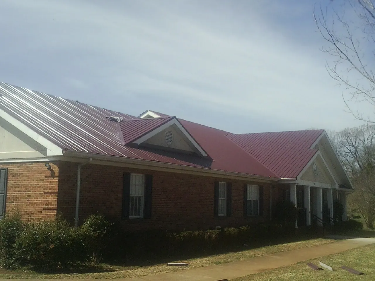 Red metal roof with gabled entries on a long brick building, from a Hail Damage Roof Repair job in Watkins