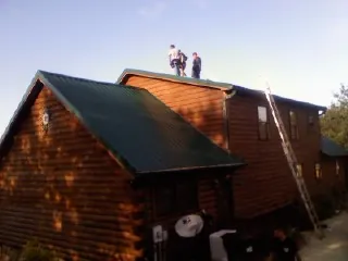 Crew on the ridge of a green metal roof on a two story log home in Watkins