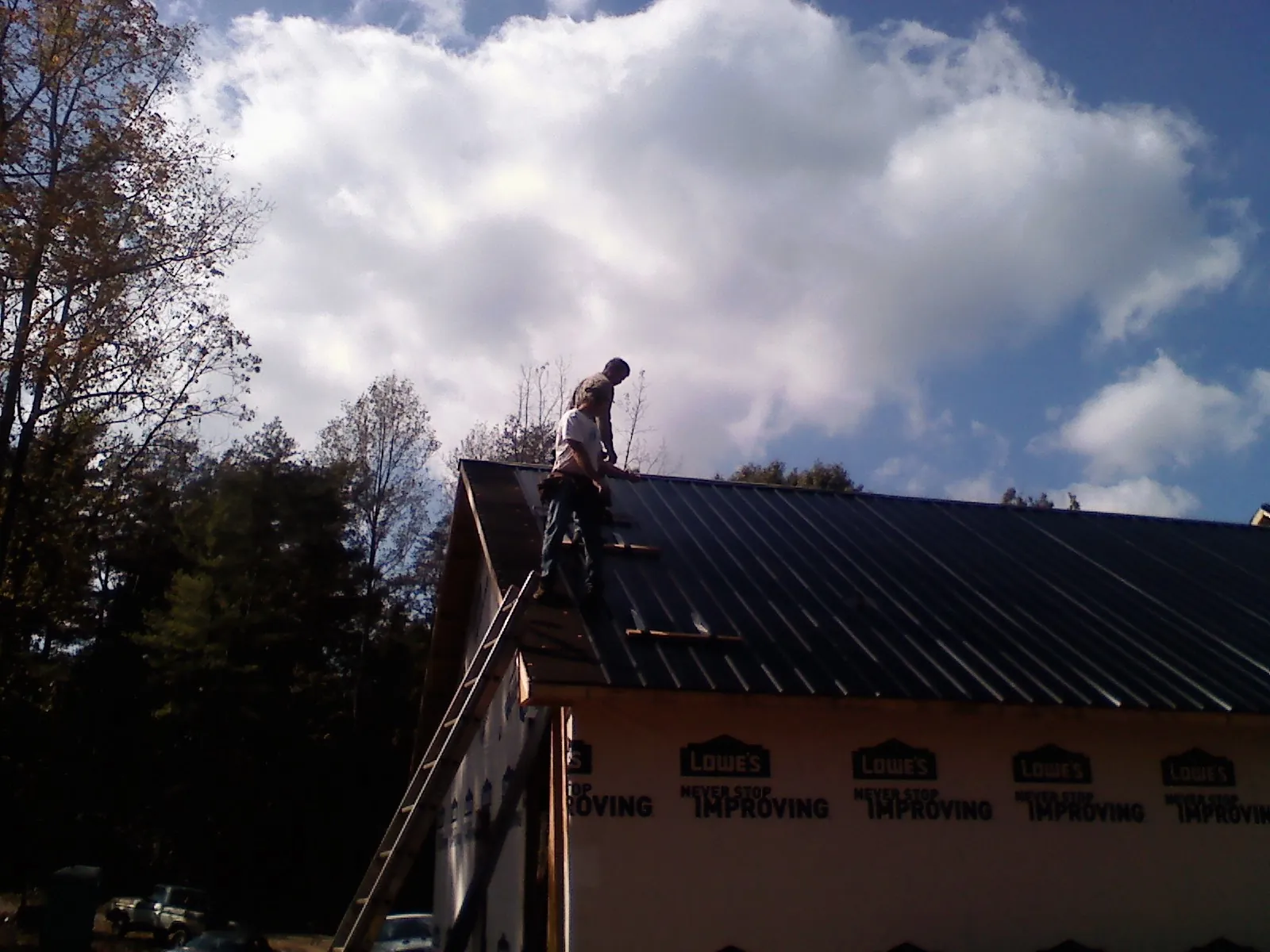Roofer fastening dark metal panels high against a cloudy sky, from a Roof Inspection job in Watkins