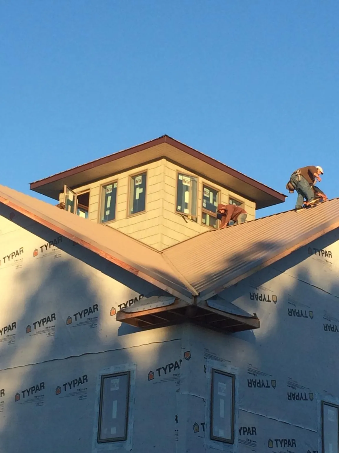 Roofers working around a rooftop cupola on a new metal roof at sunset — Roof Waterproofing in Watkins by Roofing Brothers